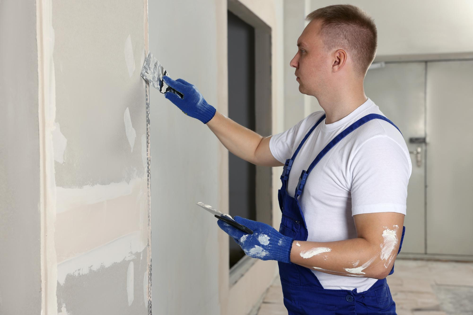 Hombre enyesado de pared con espátula en el interior